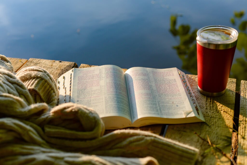 Open Bible resting on a wooden table beside a warm drink outdoors